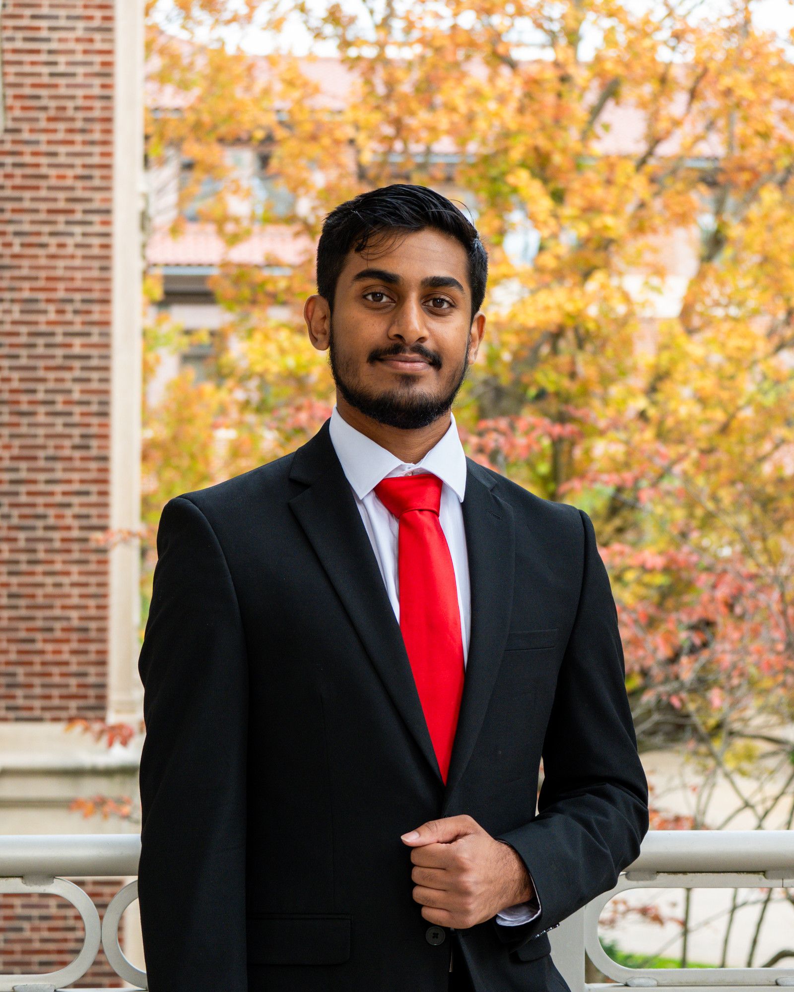 Gautam Nambiar standing outside in a dark suit and red tie.